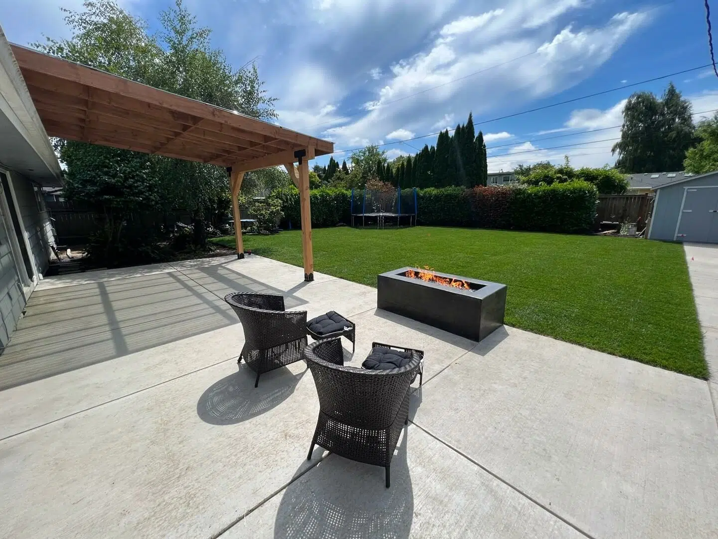 Concrete backyard patio featuring a custom pergola, fire pit, and outdoor seating area.